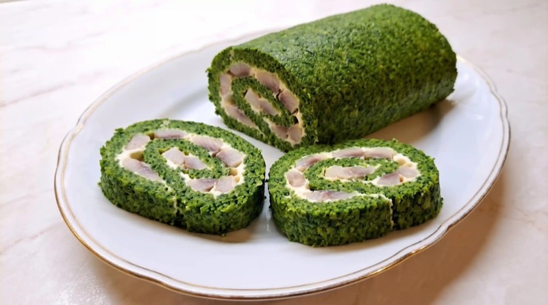 Яркий шпинатный рулет с нежной начинкой из маскарпоне и кусочками слабосоленой сельди на белой тарелке